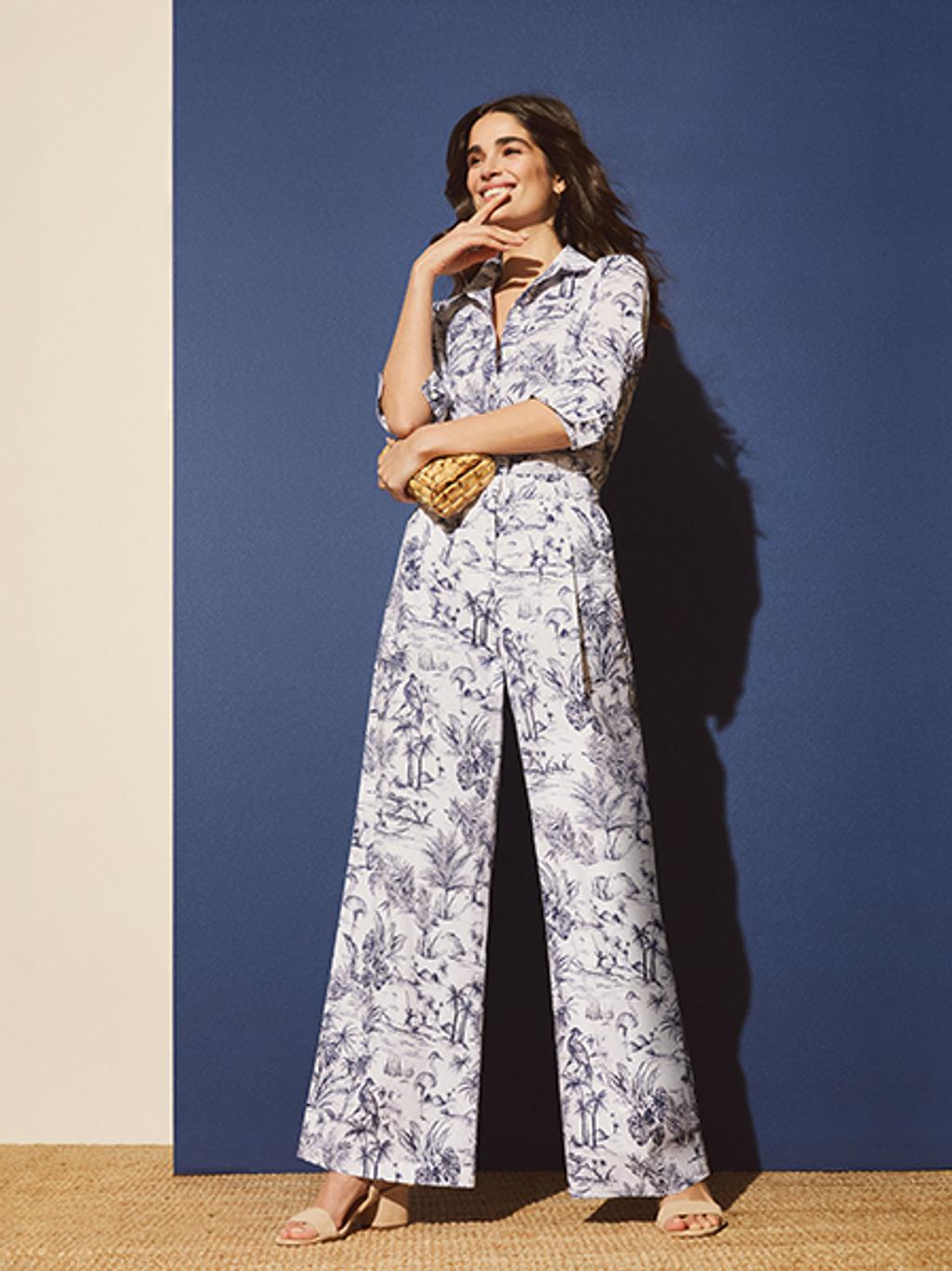 Model in a matching navy and white top and pants with tan colored heels. She is also holding a wicker handbag looking away from the camera.