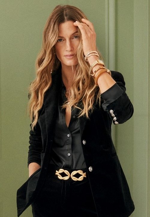 woman standing in front of green wall wearing black velvet blazer and satin button down shirt