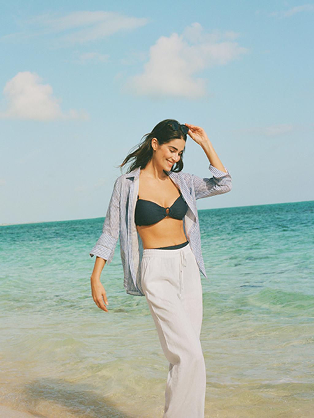 Model wearing navy bikini, striped button-down shirt, and linen pants.