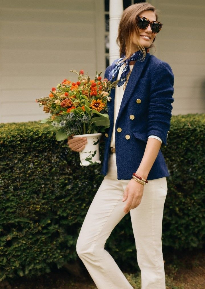woman walking outside carrying pot of flowers wearing cream jeans and a navy boucle blazer