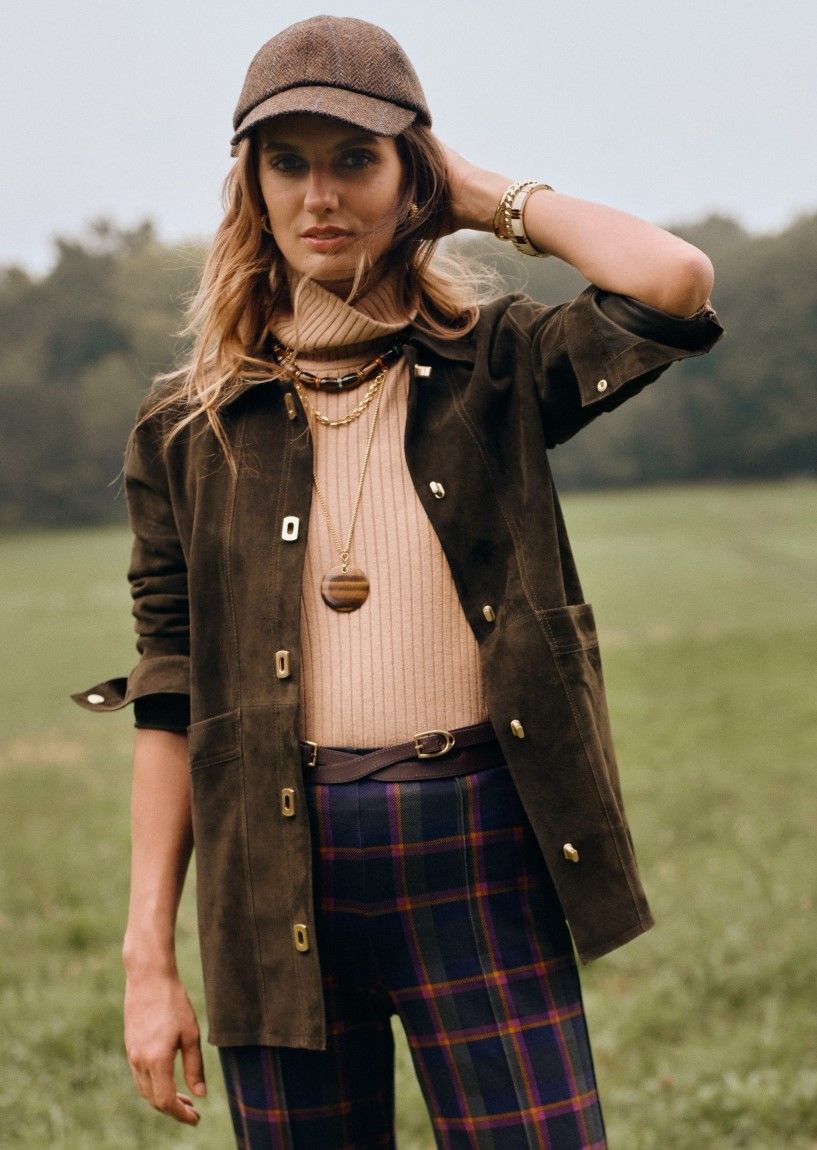 woman standing outside in a field wearing olive suede jacket with camel ribbed turtleneck and plaid pants