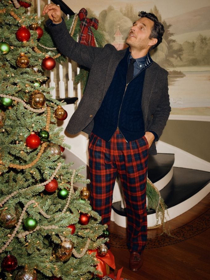 man in red tartan pants putting ornament on the christmas tree