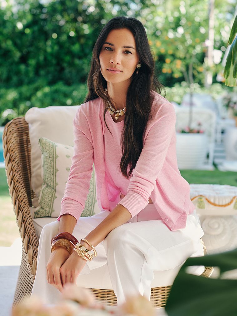 woman seated on a couch wearing a pink cardigan and linen pants. 