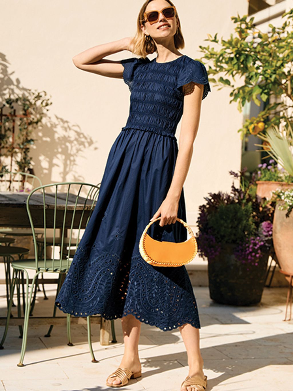 Model in navy eyelet dress with bag and slides.