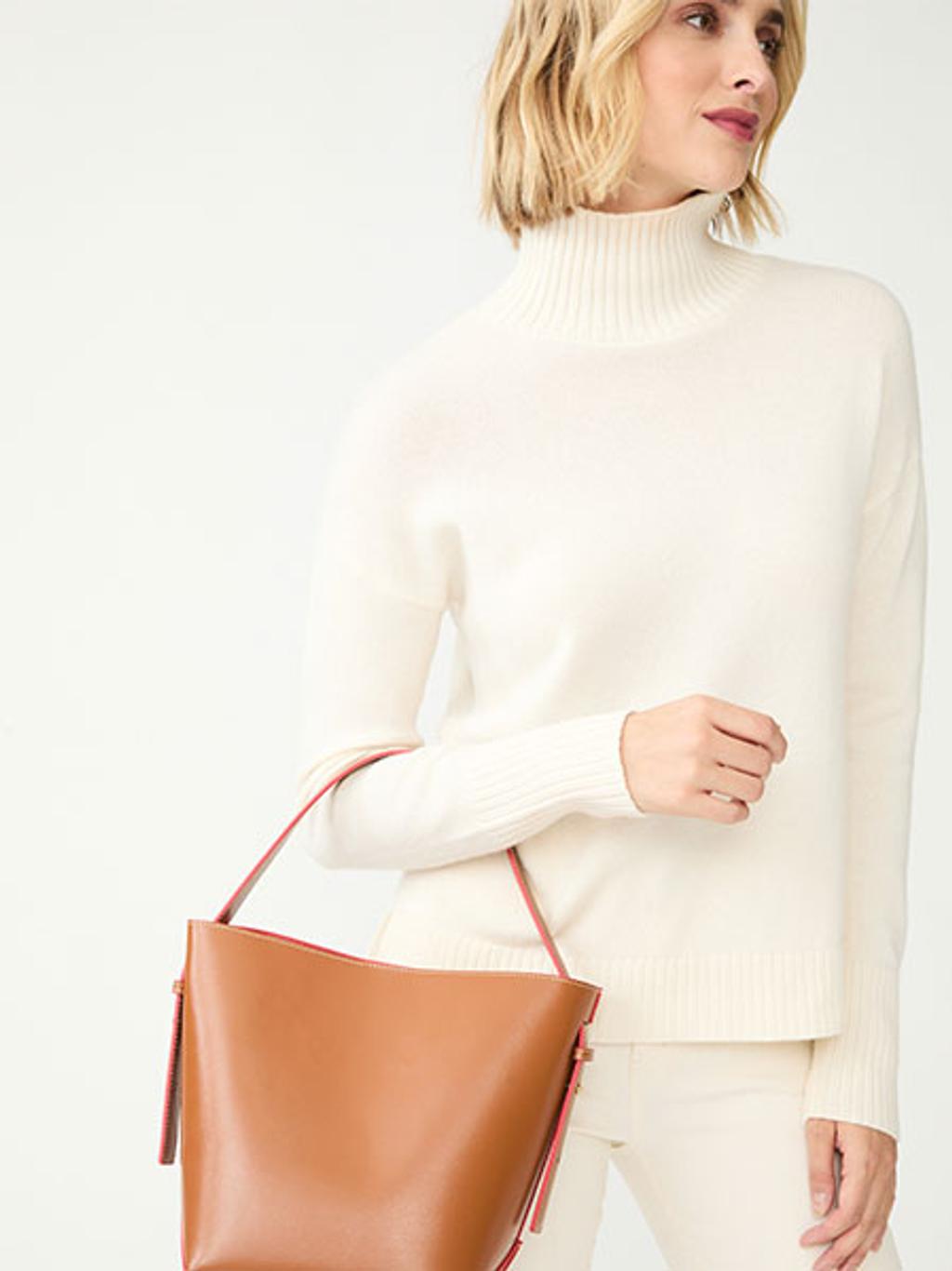 Model wearing a white turtleneck holding a brown leather bag
