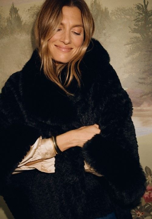 Woman standing against a mural painted wall wearing black faux fur cardigan