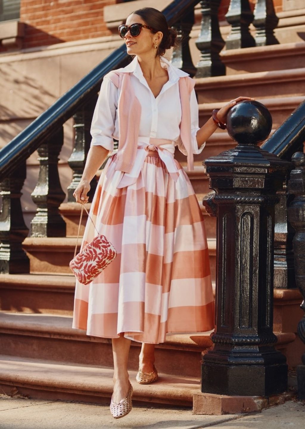 Woman walking down brownstone steps wearing white button down shirt and an oversize pink and white gingham silk taffeta ball skirt