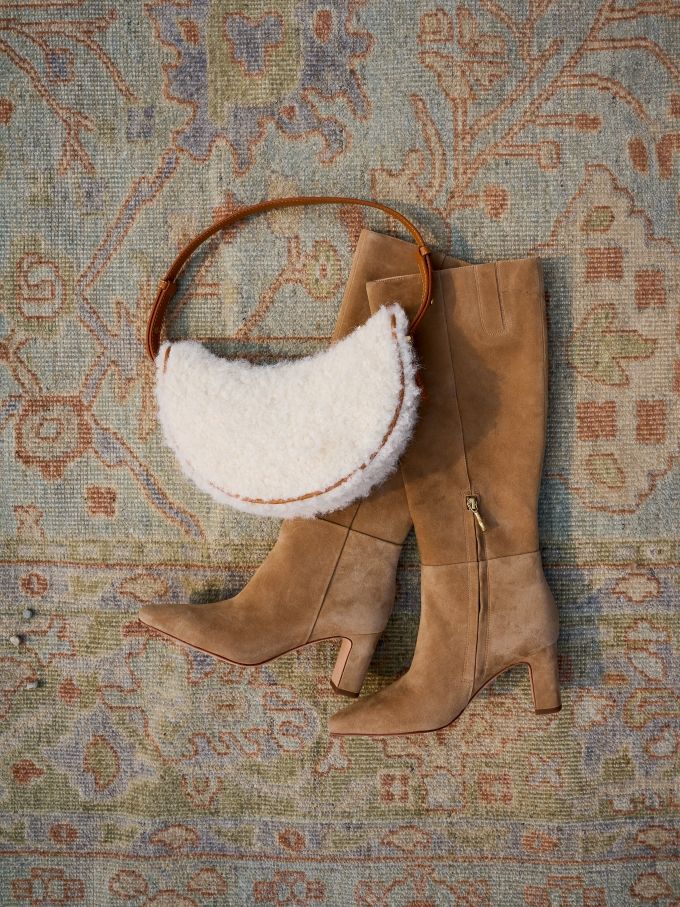 womans tall light tan suede boots with white shearling shoulder bag on geo pattern carpet