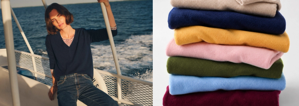 A woman in a navy top and jeans on a boat, next to a stack of colorful folded sweaters.