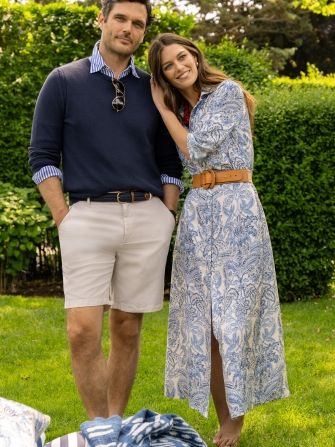 man and woman on a lawn, her wearing blue paisley printed shirtdress, he is in navy crewneck sweater and khaki shorts
