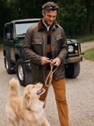 man walking away from jeep outside wearing dark tan pants with olive quilted jacket and walking a golden retriever