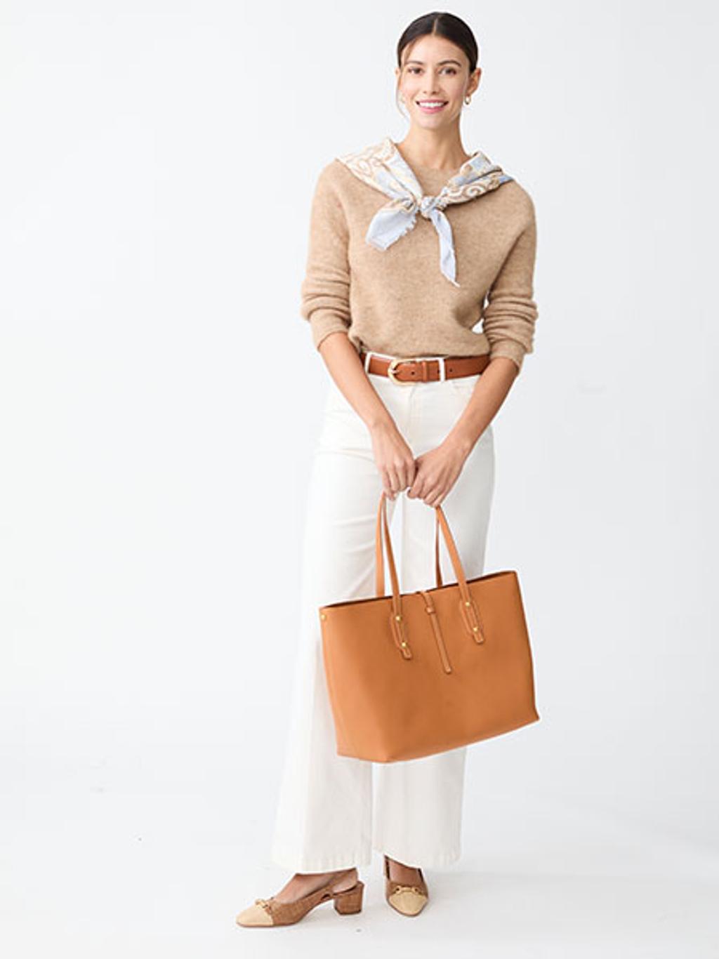 Model in tan sweater, white jeans, and holding a brown leather tote Model in tan sweater, white jeans, and holding a brown leather tote