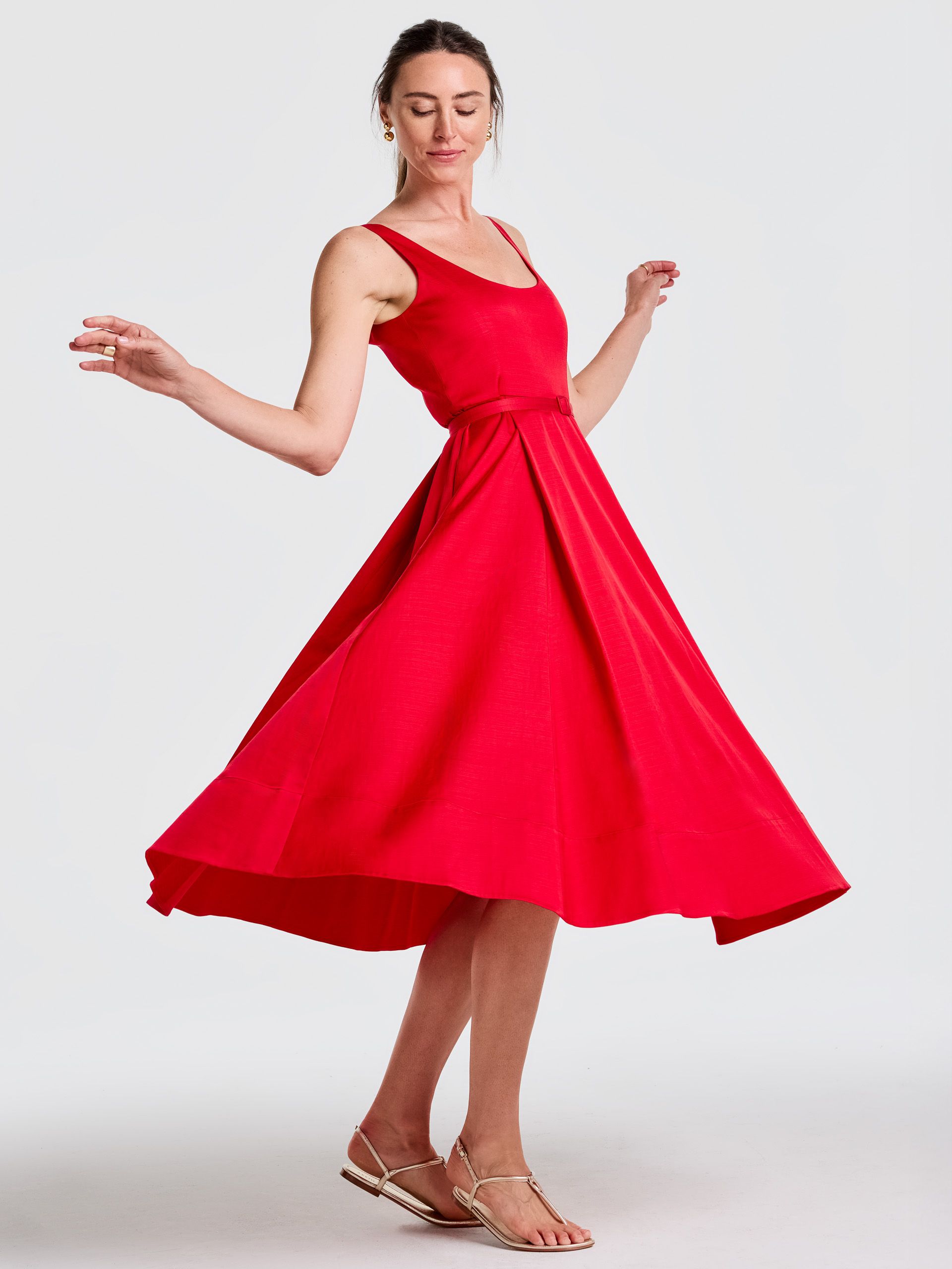 A woman in a red full-skirted dress twirls, wearing gold flat sandals.