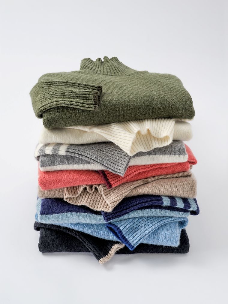 A stack of neatly folded colorful sweaters, some with stripes.