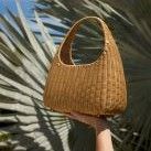 natural wicker top handle bag lifted in air with palm leaves in background