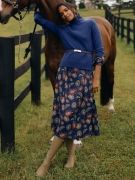 woman standing with horse in field by a fence, wearing dark blue cashmere turtleneck layered over a blue floral printed dress