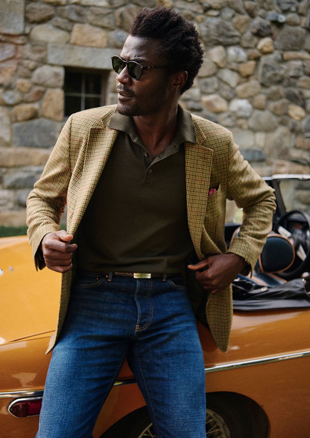 Male model wearing a houndstooth blazer, sweater, and jeans