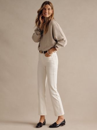 woman wearing off white jeans with loafers and a tan chunky turtleneck sweater