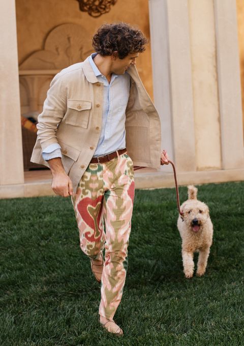 man running across a lawn with a dog wearing multi color ikat pattern pants and light beige jacket