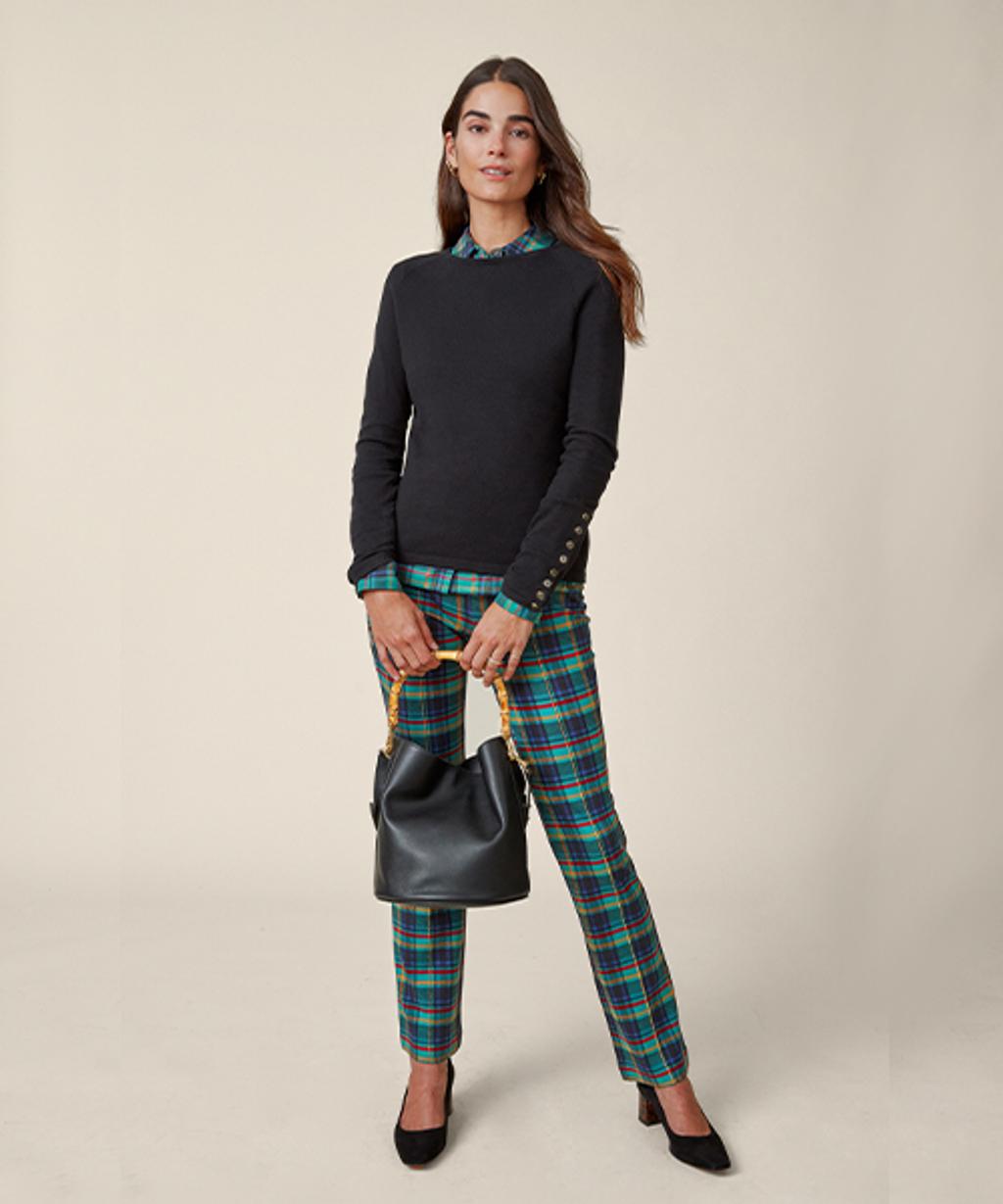 Model wearing tartan pants and shirt, crewneck sweater, suede pumps, and leather top handle bag.