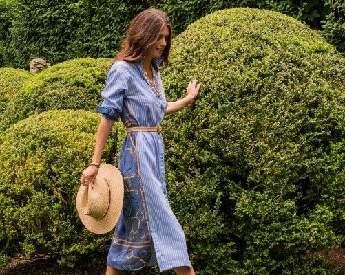 woman walking in a garden outside wearing a blue stripe shirtdress with equestrian printed back
