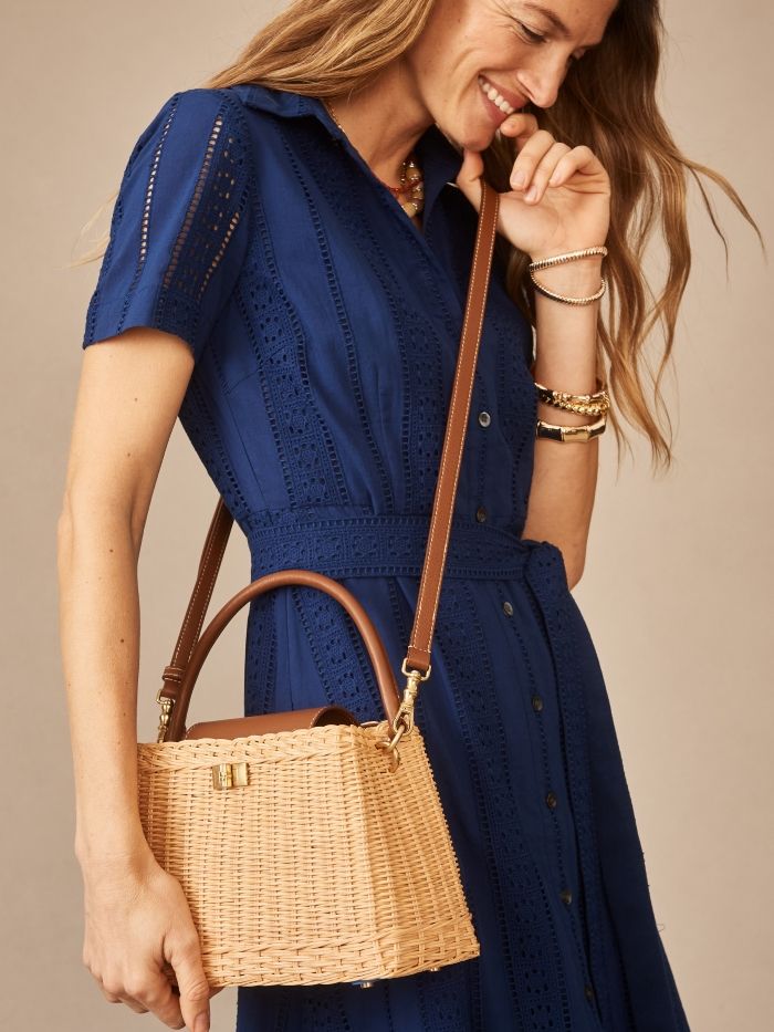 woman wearing a navy dress and a wicker top handle bag with leather crossbody strap
