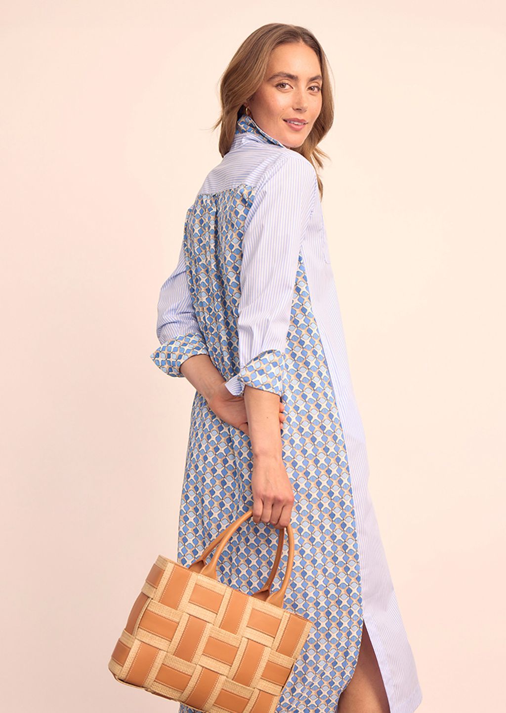 Model wearing blue and white striped shirt dress with geometric print on the back and holding a wicker handbag.
