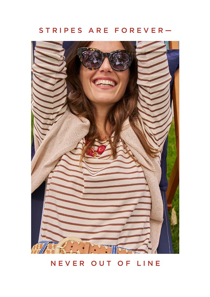 Woman sitting in cabana chair smiling in a brown striped tee. 