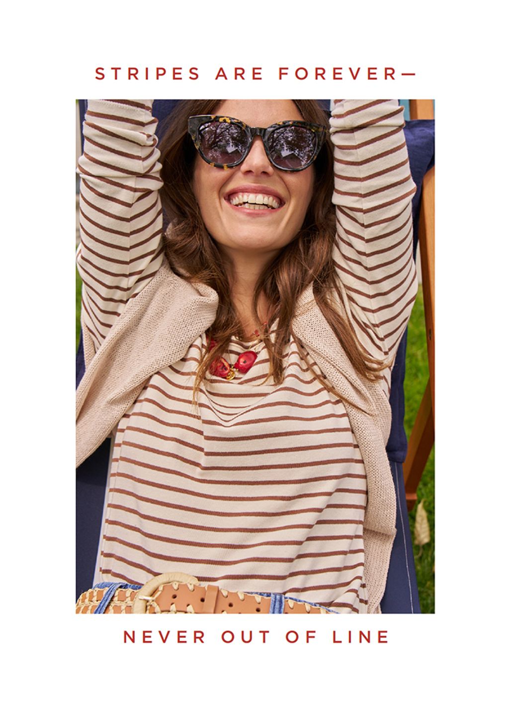 Woman sitting in cabana chair smiling in a brown striped tee. 