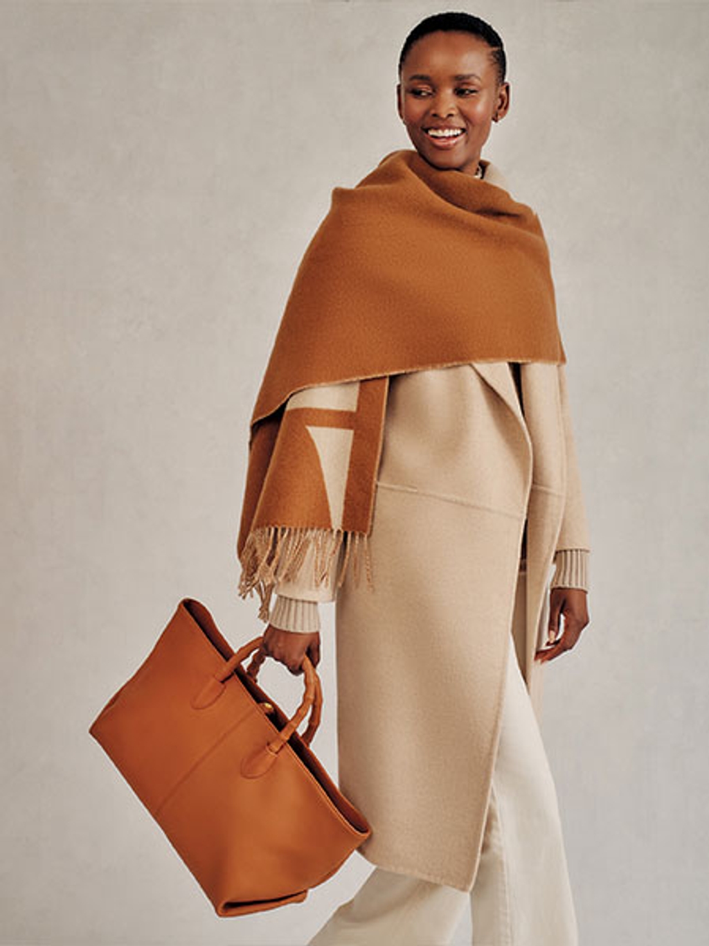 Model in a wrap coat carrying a leather tote bag Model in a wrap coat carrying a leather tote bag