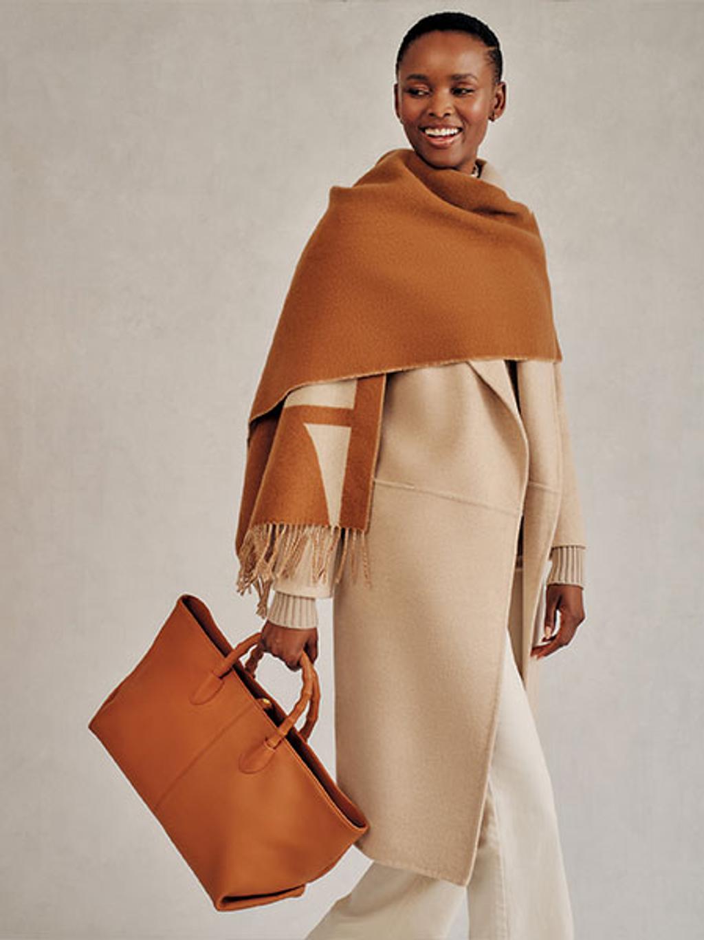 Model in a wrap coat carrying a leather tote bag Model in a wrap coat carrying a leather tote bag