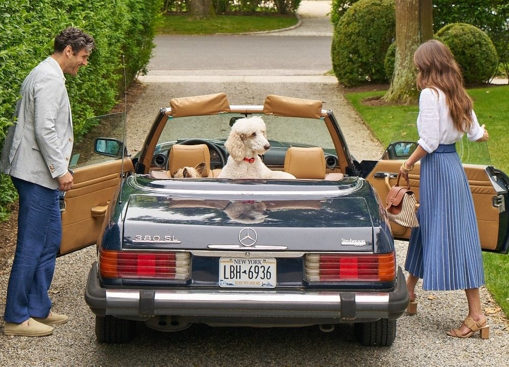 man and woman outside leaving in a mercedez convertible with poodle in the backseat