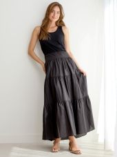 woman leaning against a white wall wearing a black tiered maxi skirt and a solid blank tank top