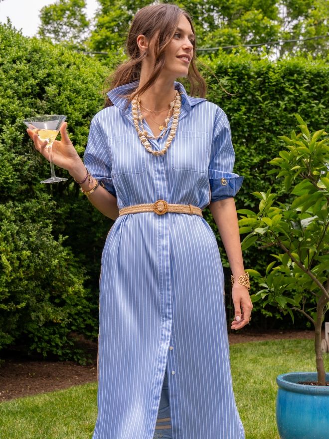 woman standing outside in blue and white pinstripe shirtdress holding a cocktail