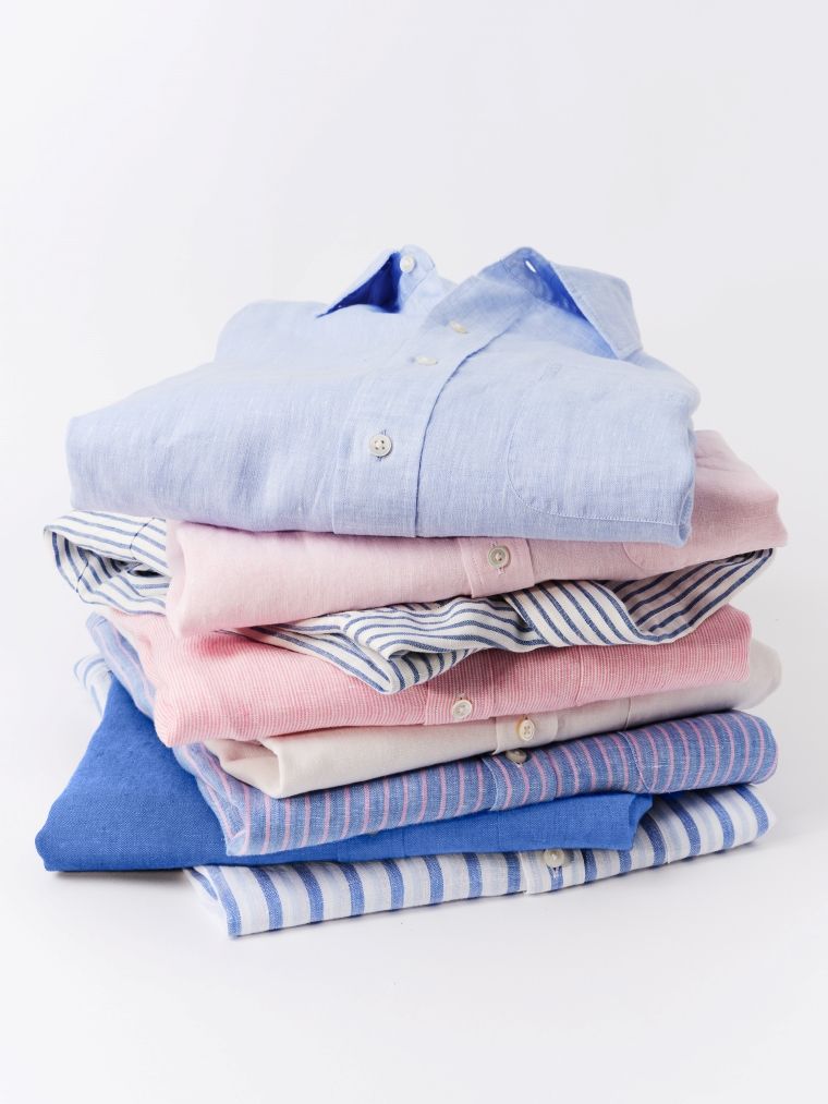 A stack of folded shirts in blue, pink, and white, some striped.