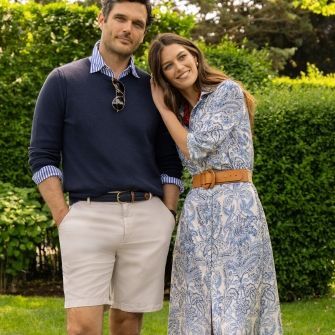 man and woman on a lawn, her wearing blue paisley printed shirtdress, he is in navy crewneck sweater and khaki shorts