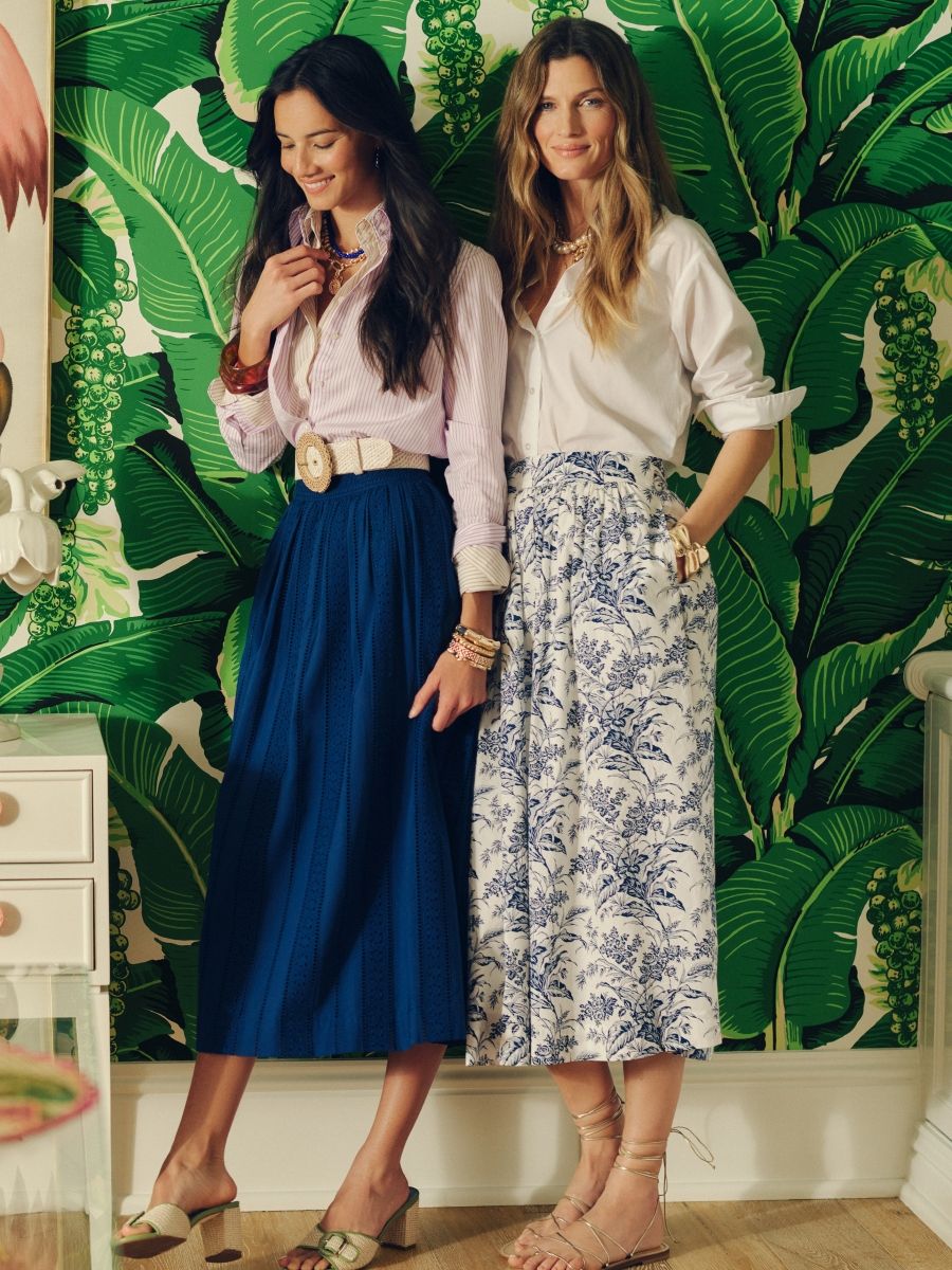 two women standing in room with palm wallpaper wearing full midi skirts, one in navy, one in toile