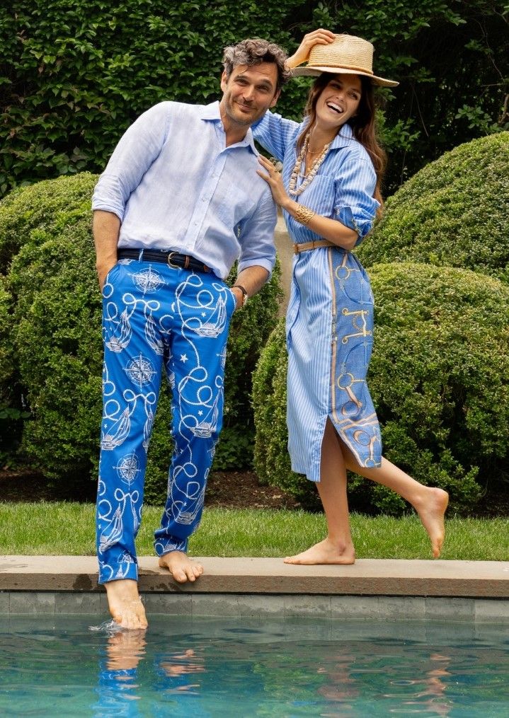 woman and man standing by a pool, her wearing blue stripe shirtdress with printed back and him wearing blue nautical printed pants
