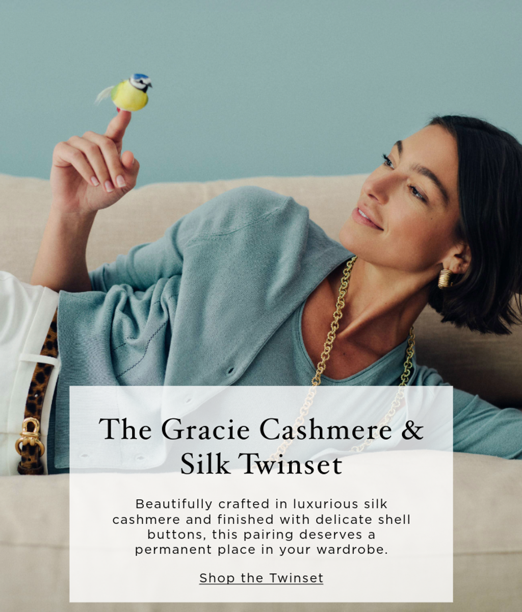A woman in a light blue twinset lies on a couch, smiling at a small yellow and blue bird perched on her finger. An overlay promotes "The Gracie Cashmere & Silk Twinset."