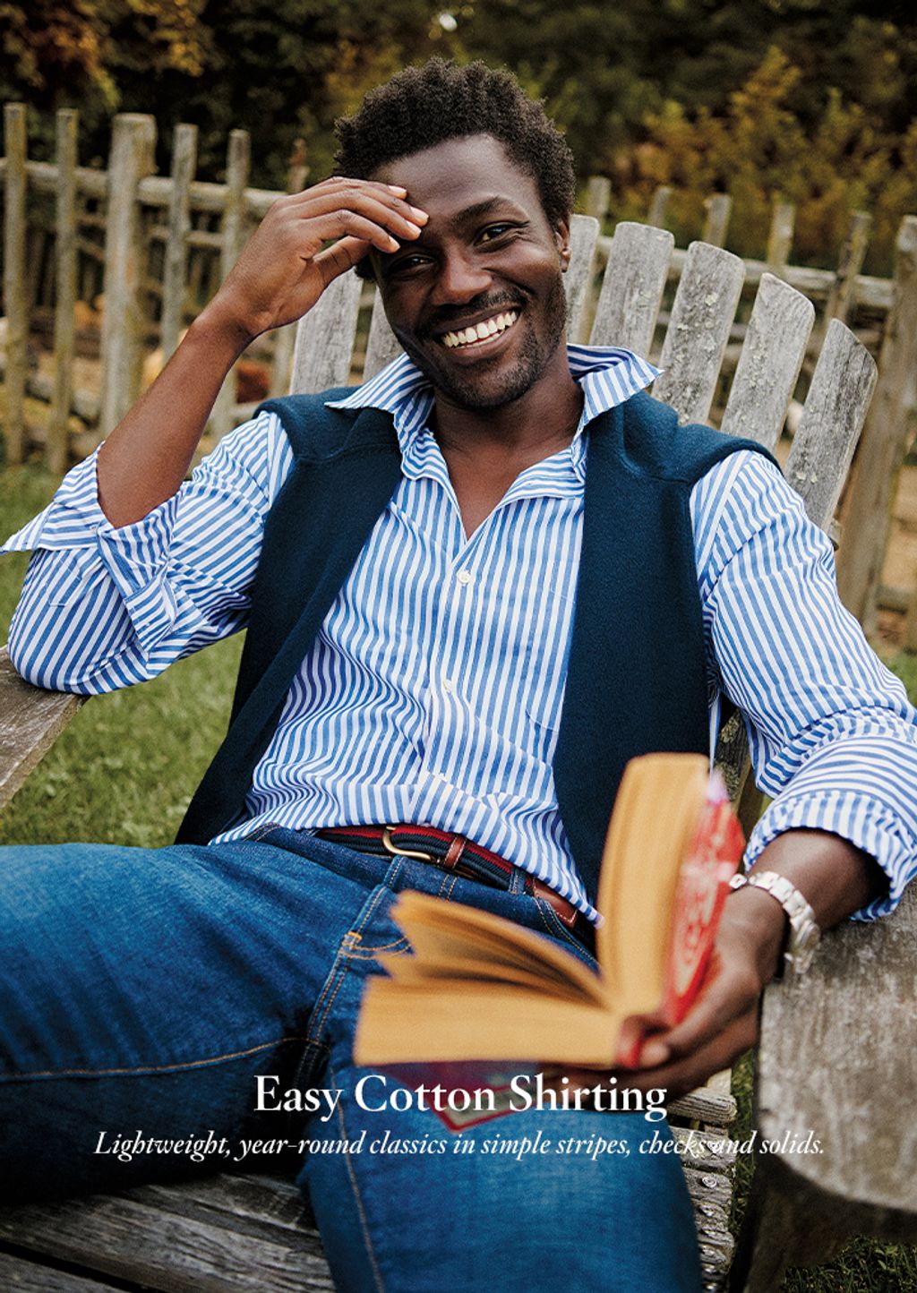 Male seated outside wearing a blue and white striped button down shirt and jeans.