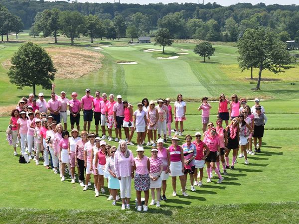Large group of women and girls wearing pink clothing arranged in a heart formation on a golf course