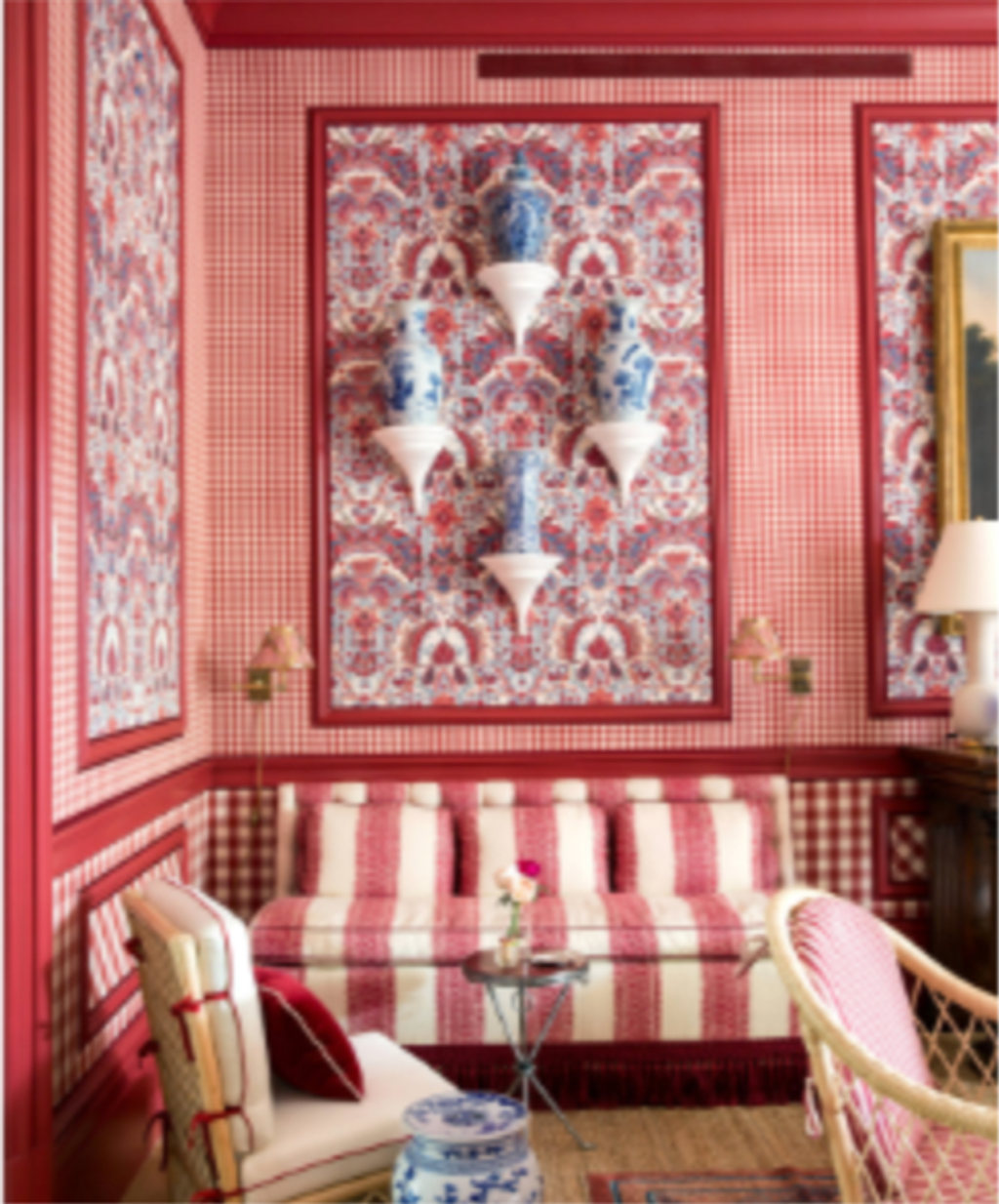 A room richly decorated in red and white patterns, featuring a striped daybed, blue and white urns on wall sconces, and gingham wallpaper.