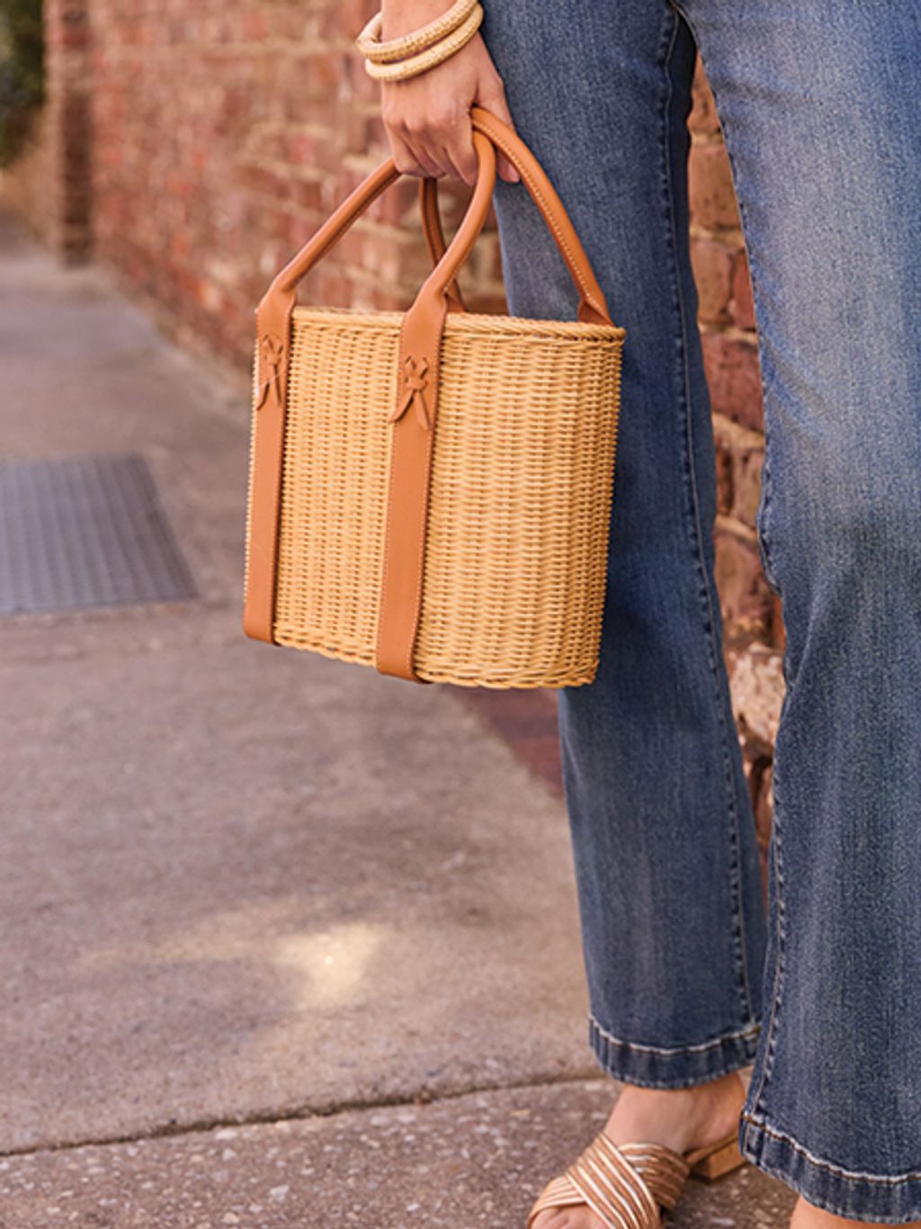 Cropped shot of model holding wicker tote, wearing jeans and a white top