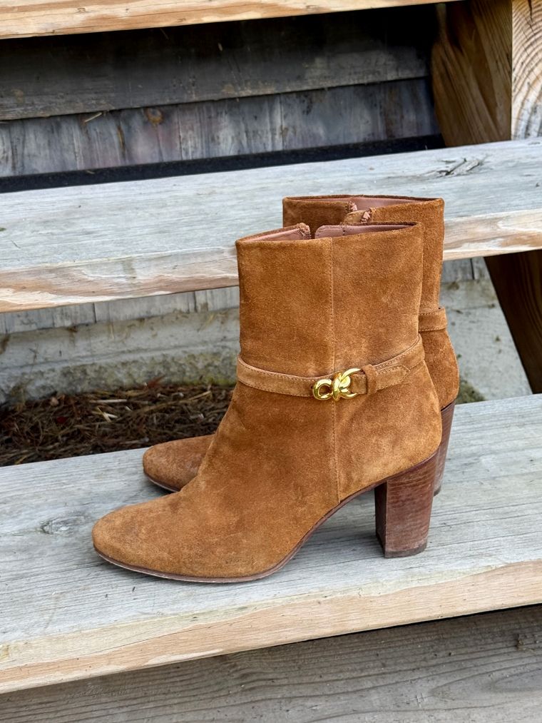 Brown suede ankle boots with gold buckle detail on a wooden surface.