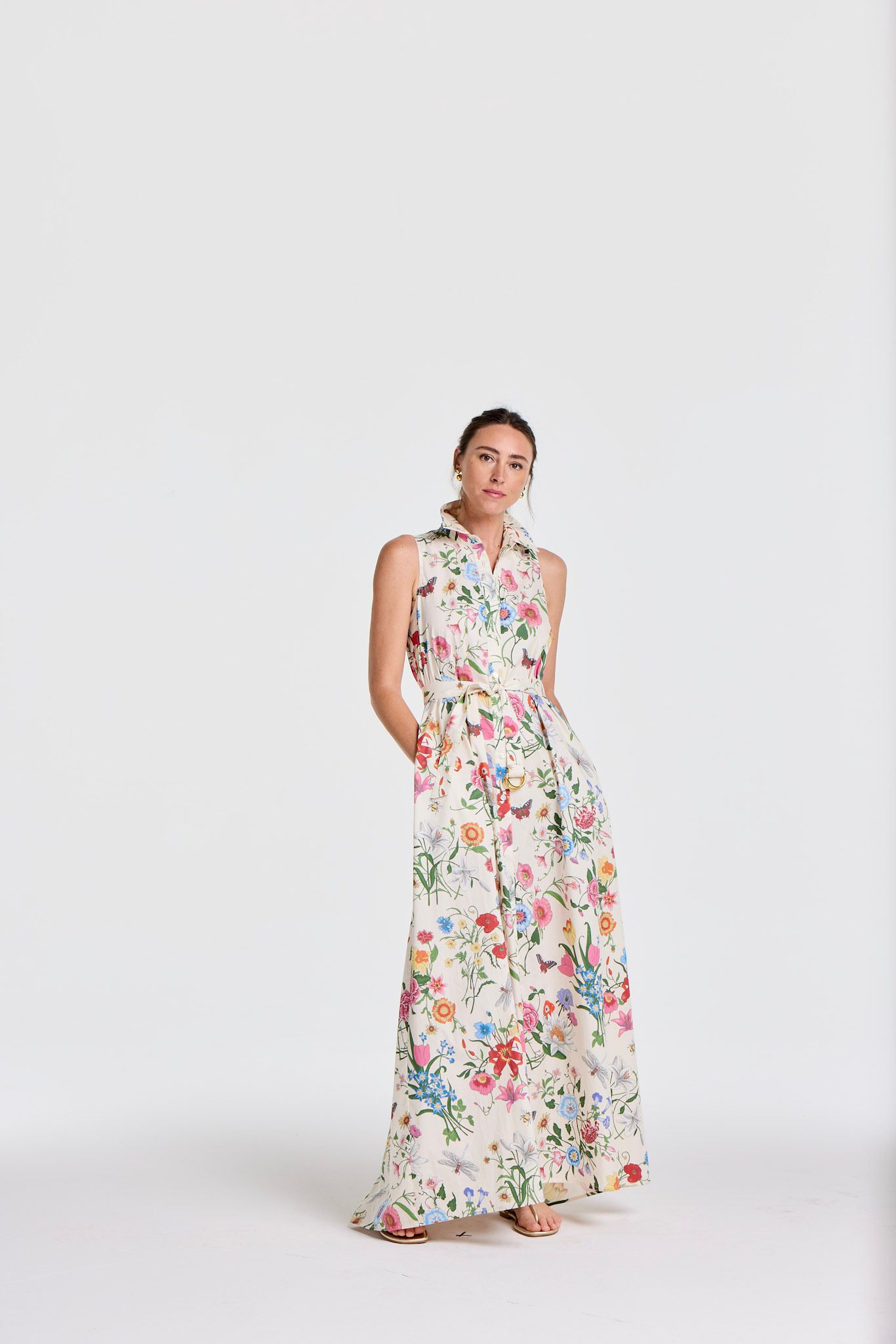 A woman poses in a white sleeveless, collared maxi dress with a vibrant floral and butterfly print.
