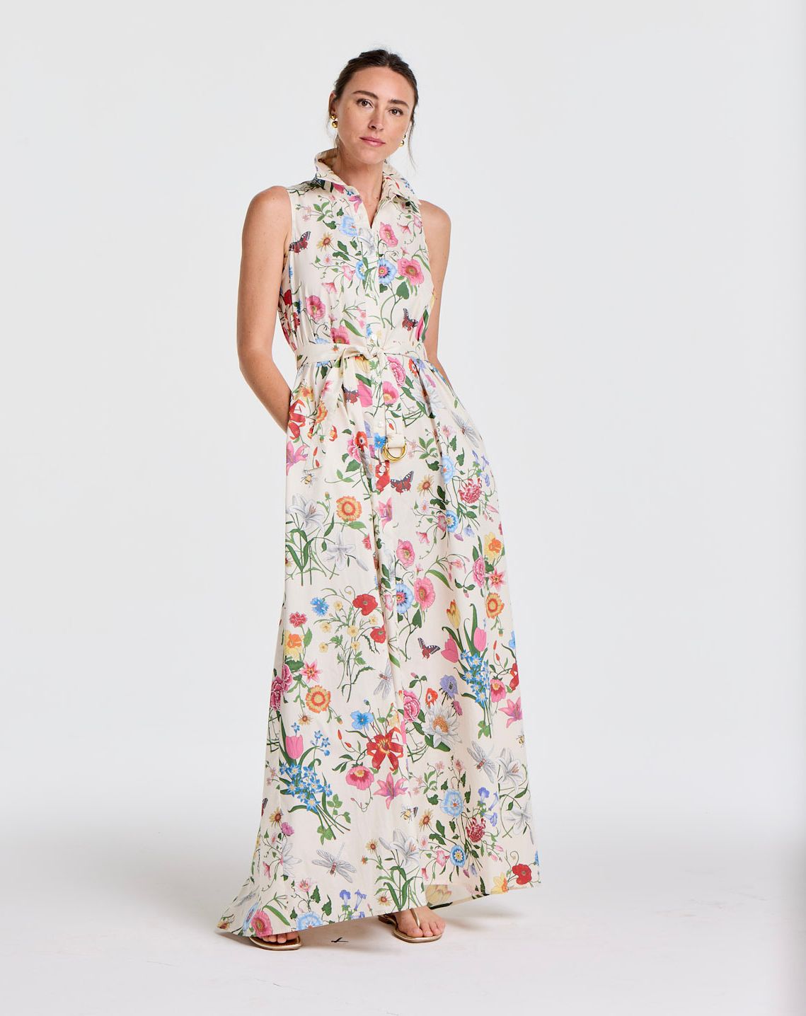 A woman poses in a white sleeveless, collared maxi dress with a vibrant floral and butterfly print.