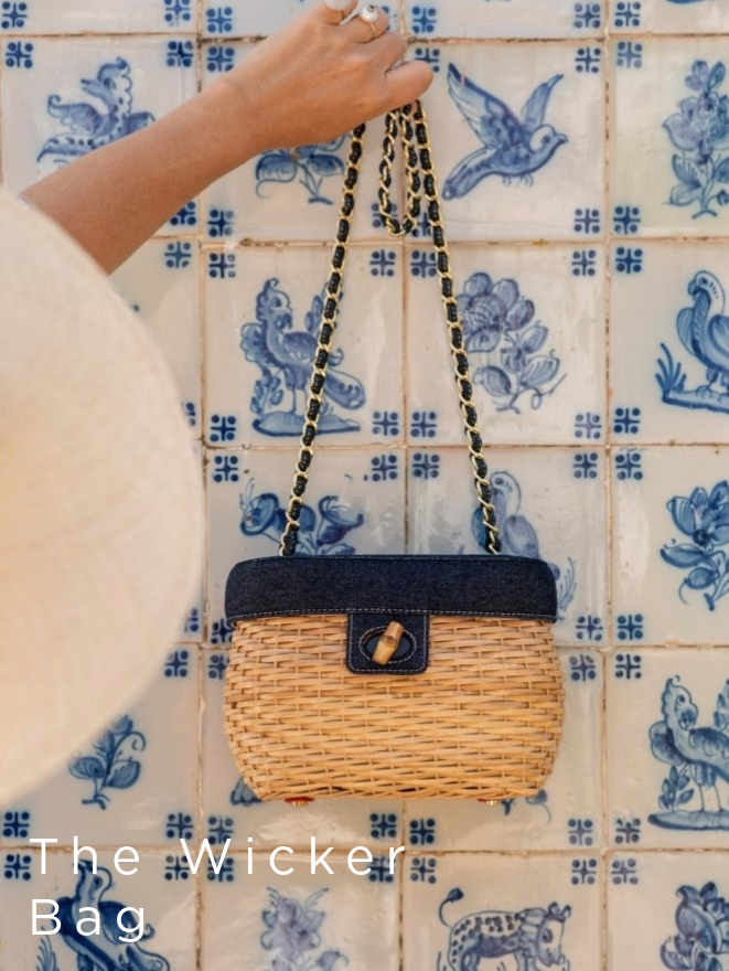 woman's hand holding up a wicker bag, with denim navy top and bamboo turnlock against a blue mosaic tile backdrop