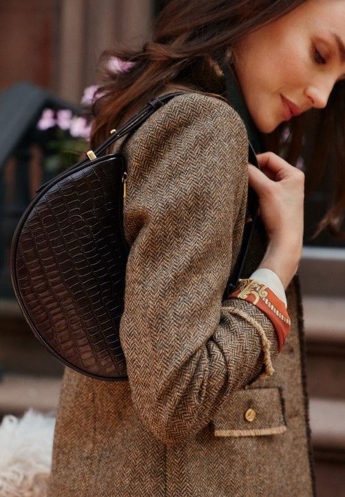 cropped image of woman holding brown leather half moon shoulder bag with turnlock closure, standing in front of white studio backdrop