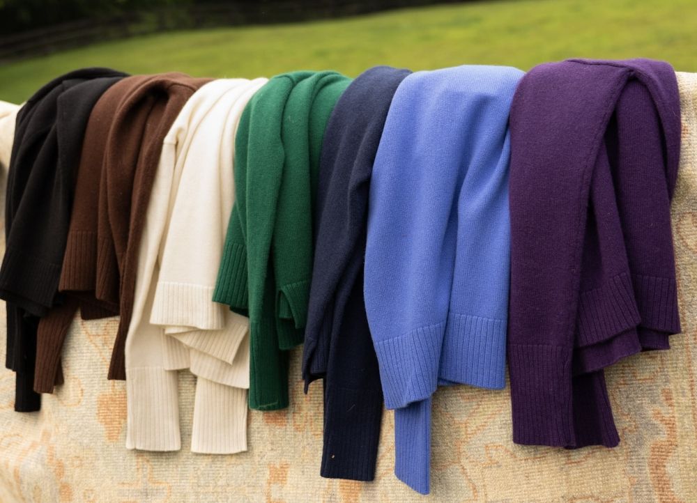 group of womens cashmere sweaters, in various colors, arranged outside draped over geo pattern rug