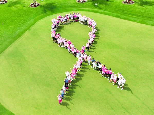 Participants at a breast cancer awareness golf event forming a human ribbon symbol, photographed from above